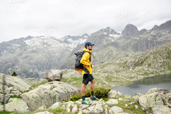Fototapeta Young man standing on a rock with mountain background