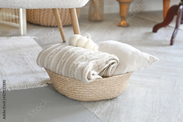 Fototapeta Folded knitted beige linen blanket and pillow inside a rustic woven backet. Wicker basket with cozy plaid. Home interior