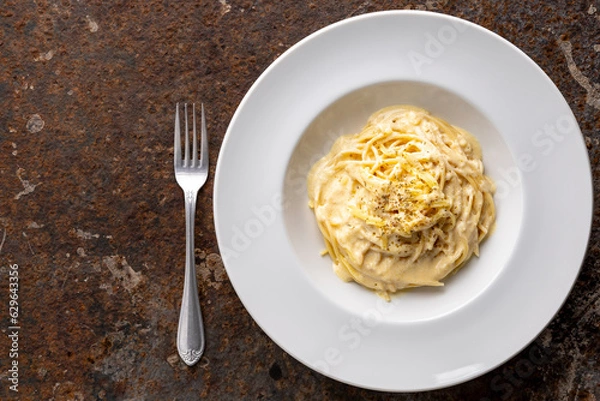 Fototapeta spaghetti carbonara with cream sauce in classy white circle ceramic plate beside fork on rusty texture background with copy space for text, top view, flat lay
