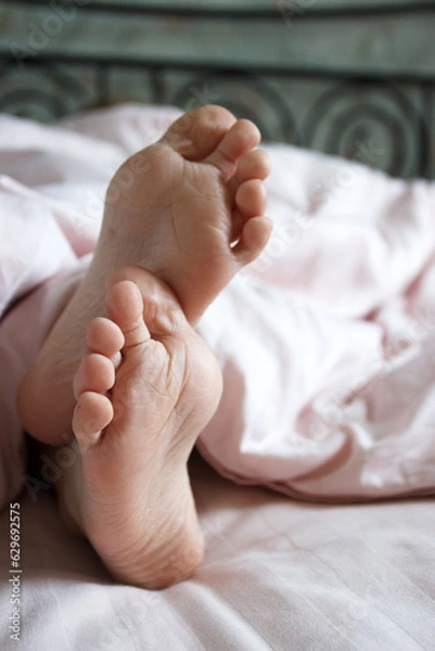 Fototapeta Feet under a light blanket on the bed. Concept of sleeping or waking