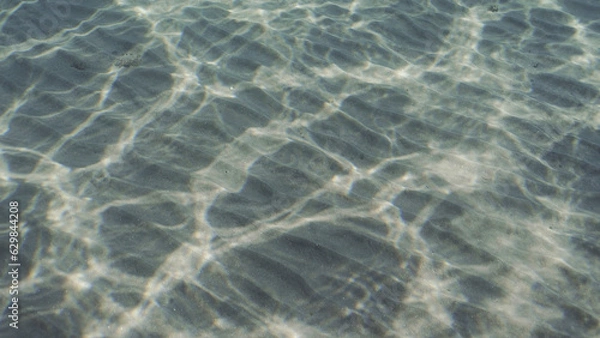 Obraz Glare of sun plays on sandy bottom in shallow water. Top view on sandy seabed in shallow water with diagonal lines of sand and sun glare on its surface in brightly suny day, Red sea, Egypt