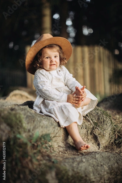 Fototapeta Little girl wearing hat, sitting bootless in the countryside