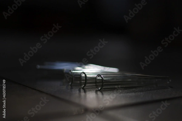 Fototapeta Several empty glass chemical test tubes that cast shadows and glare on a gray surface in a dark room with low light