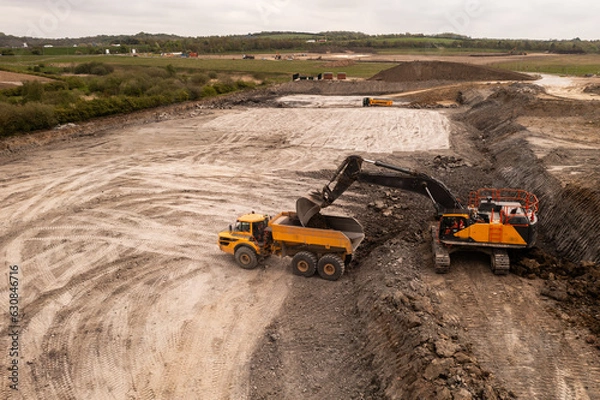 Fototapeta Aerial view above a digger loading a dumper truck on a brownfield site in the construction industry