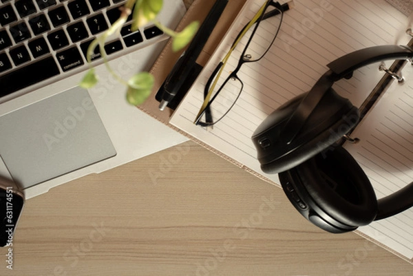Fototapeta Top view of office Workplace with open laptop, a blank open note book, a smart phone ,a pen, a specs and a head phone on a wooden desk