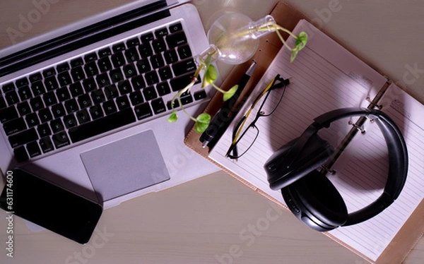 Fototapeta Top view of office Workplace with open laptop, a blank open note book, a smart phone ,a pen, a specs and a head phone on a wooden desk