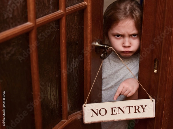 Fototapeta An angry child closes the door to his room and points to a sign that says No entry. The child does not let her parents into the room. Upbringing problems, the conquest of personal space by children