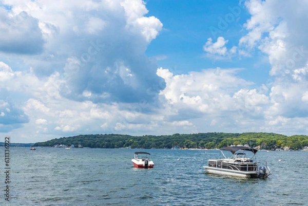 Fototapeta A pontoon boat and pleasure boat anchored in a large lake with white cumulus clouds and a blue sky.