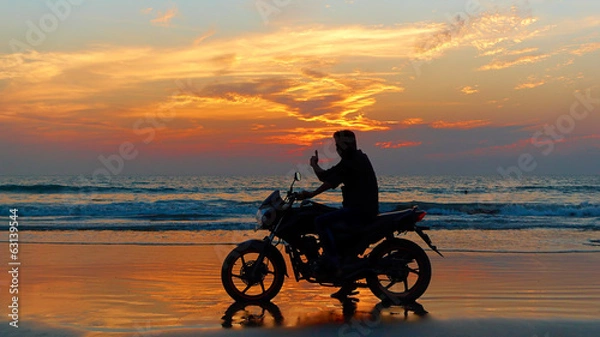 Fototapeta Motorcyclist at sunset on the beach.