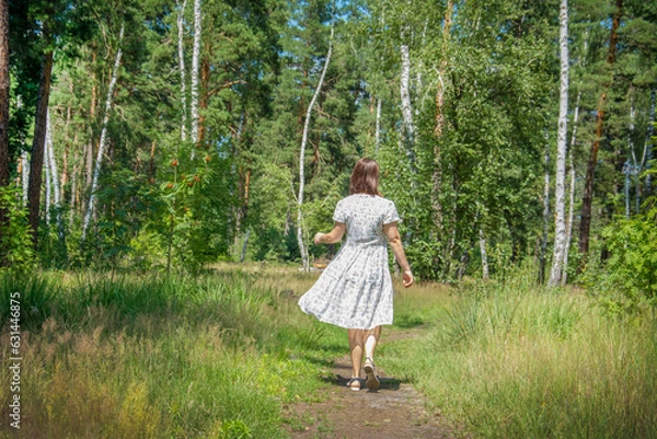 Fototapeta In the summer in the forest, a woman walks through the forest.