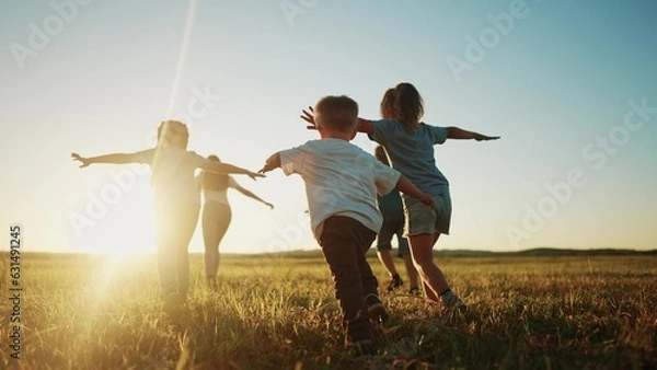 Fototapeta Dzieci biegają w parku o zachodzie słońca. Przyjazne rodzina dzieci Camp Kid Dream Concept. Grupa dzieci biegnie na trawie w Rays Fun of the Sun Silhouette. Concept
