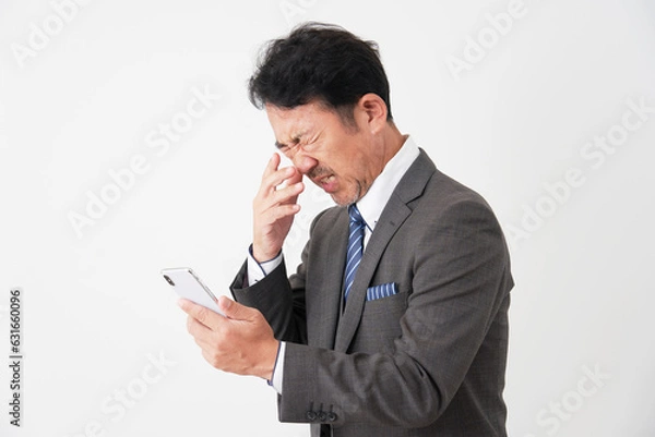 Fototapeta スマートフォンを持って悩むミドルエイジのビジネスマン　白背景