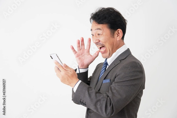Fototapeta スマートフォンを持って驚くミドルエイジのビジネスマン　白背景