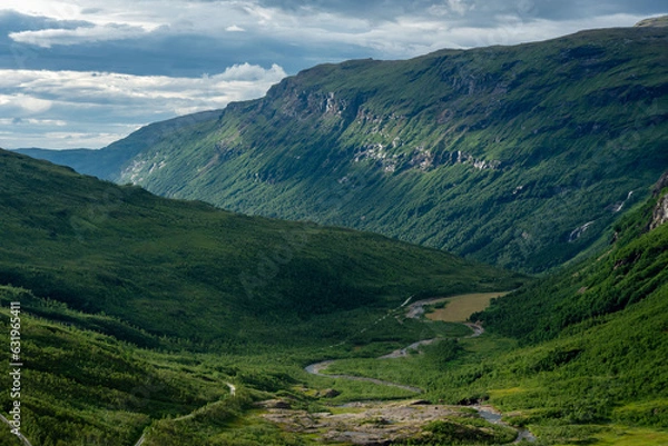 Fototapeta Sunlit green mountain slopes on the way up to Rabothytta, Okstindan, Hemnes, Helgeland, Northern Norway. Green mountains of Nordnorge. Sunny patches on dark mountains. Cloudy dramatic skies and light.