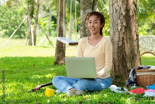 Fototapeta Asian student girl is studying  by laptop in nature with tree. Asian student is happy in study online and drinking coffee. Education in online life concept. Study Online in vacation..