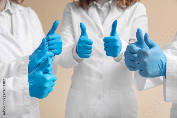 Fototapeta Doctors in medical gloves showing thumbs-up on beige background, closeup