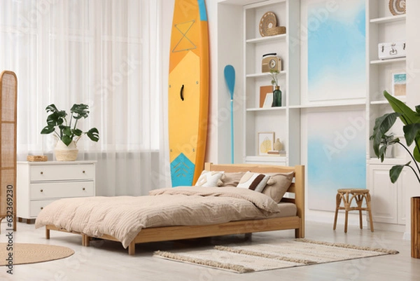 Fototapeta SUP board, bed and furniture in room. Interior design