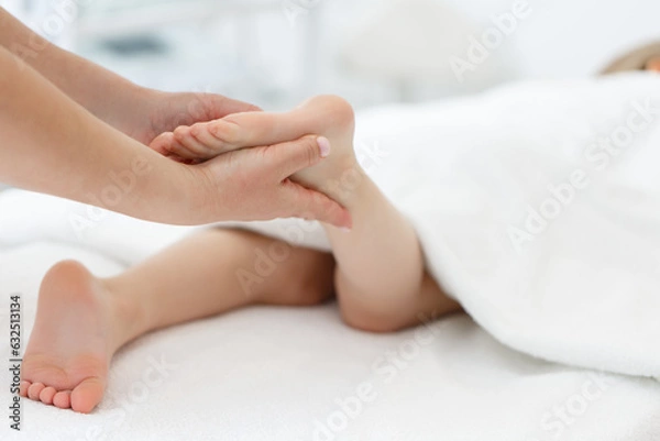 Fototapeta Doctor or a nurse massages the legs of a small child with her hands. Close-up of baby's foot