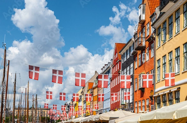 Fototapeta Waving danish flags above touristic street with colorful buildings in Nyhavn, Copenhagen in Denmark.