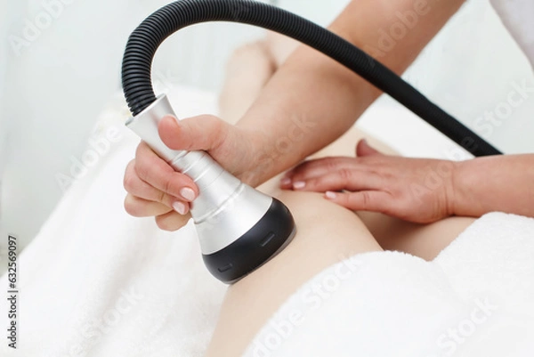 Fototapeta RF body cavitation lifting procedure in a beauty salon. Ultrasound therapy to reduce fat and elasticity of the skin. Cosmetic ultrasonic anti-cellulite massage close-up