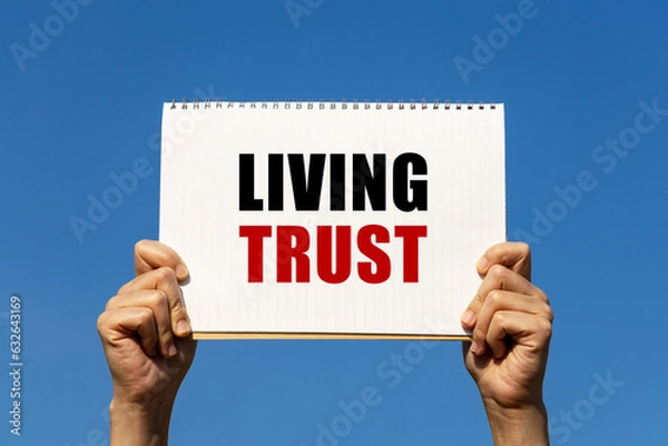 Fototapeta Living trust text on notebook paper held by 2 hands with isolated blue sky background. This message can be used as business concept about living trust.