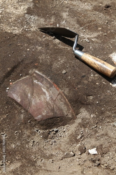Fototapeta Authentic archaeological excavation with excavated clay shard, a real artefact an an excavation trowel