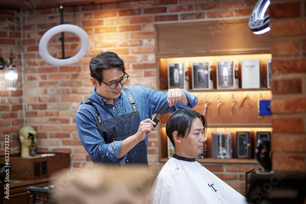 Obraz 미용실에서 미용가위로 남자 손님의 헤어컷을 하고있는 안경을 쓴 헤어디자이너