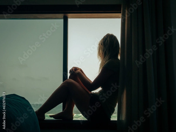Fototapeta Silhouette of a woman looking at the sea from a window