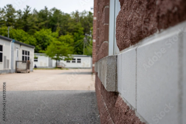 Fototapeta Red-brick school building corner with white trim and gray stone accent - pavement, school portable classrooms, trees in background. Taken in Toronto, Canada.