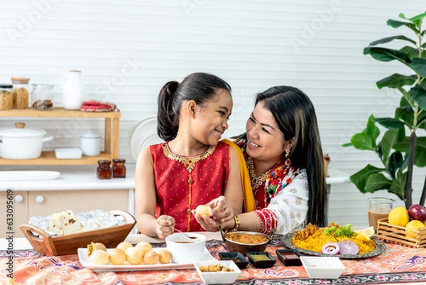 Fototapeta an Indian family, mother and daughter in the kitchen They happy together while eating Indian food, placed on the table, to family and Indian food concept.