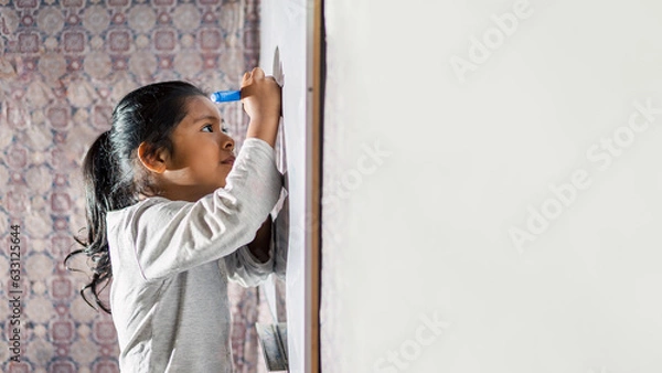 Fototapeta Niña latina sonriente y feliz, escribiendo en la pizarra de clases con plumones de colores. Espacio para texto.