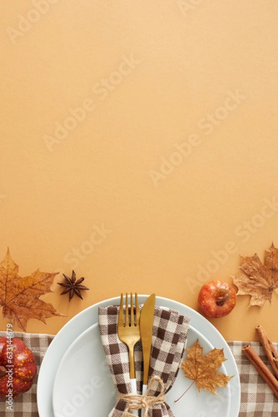 Obraz Captivating autumnal decor concept. Top view vertical shot of plate, cutlery, napkin, tablecloth, pumpkins, cinnamon sticks, anise, autumn leaves on pastel brown background with space for ads or text