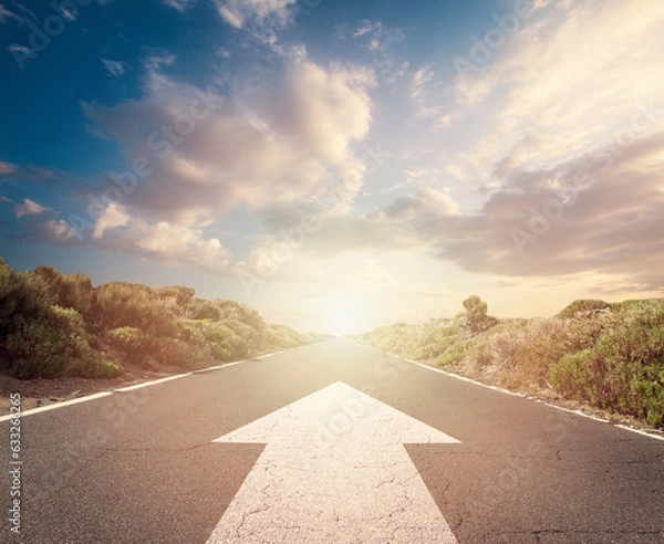 Fototapeta Success concept on an open road with white arrow at sunset sky clouds