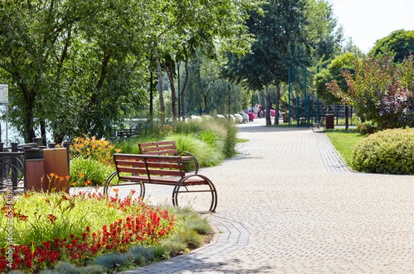 Fototapeta Rest area with bench surrounded by blooming flowers and ornamental shrubs in Kyiv, Europe. Place to rest in the city park