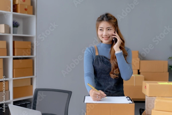 Fototapeta Happy Asian woman owner talking on the phone with customers, taking orders and preparing delivery.