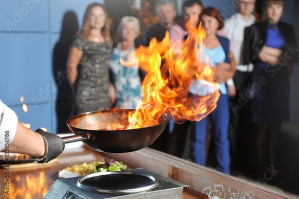 Fototapeta Cooking show for people, chef cooks, fries meat in a frying pan with fire
