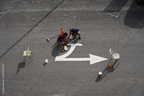 Fototapeta Two workers are repairing road sign color along with obstacles for their safety. Top view photo.