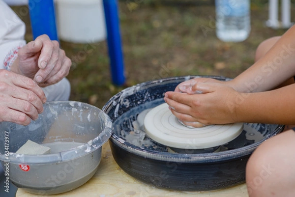 Fototapeta master class on modeling clay, creating a vase, bowl, pot on potter's wheels in the workshop. the master helps the child