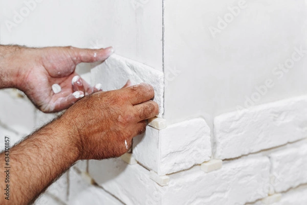 Fototapeta A man glues a white decorative stone in the form of a brick to the wall. Decor element, copy space for text
