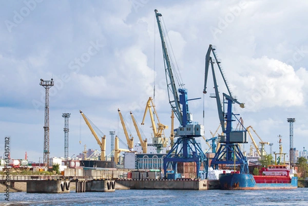 Obraz Sea cargo harbor. Port with cranes on shore. Harbor for loading ships. Container port on sunny day. Cargo harbor in summer weather. Export across ocean. Maritime logistics. Cargo transportation
