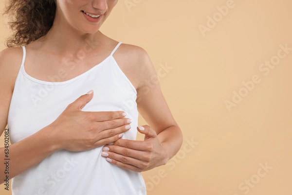 Fototapeta Woman doing breast self-examination on light brown background, closeup. Space for text