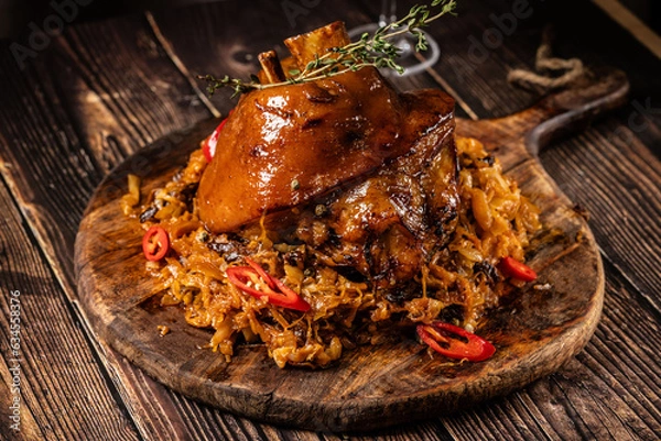 Obraz concept of German cuisine, caramelized pork knuckle in honey, with stewed cabbage. Serving in a restaurant on a wooden board with a glass of wine.