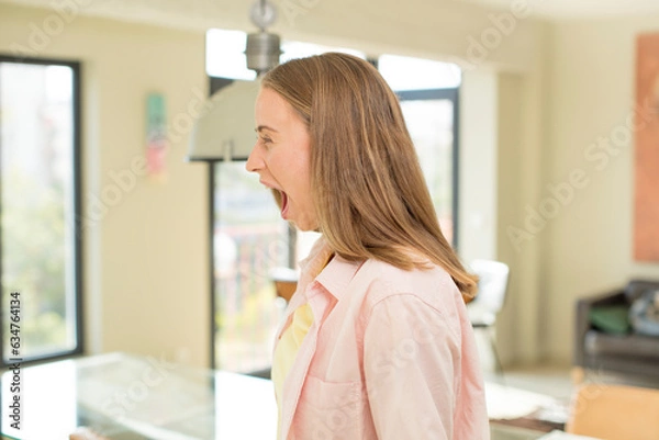 Fototapeta pretty blond woman shouting aggressively, looking very angry, frustrated, outraged or annoyed, screaming no
