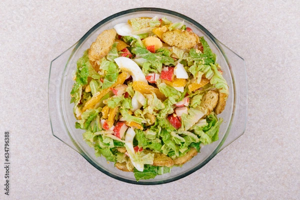 Obraz Salad with crab sticks, tomatoes, napa cabbage, eggs, lettuce and croutons in glass bowl. Top view.