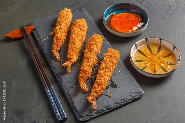 Obraz Tempura de crevettes sur une ardoise avec des sauces et baguettes sur un fond noir. Cuisine japonaise.