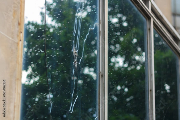 Fototapeta Broken window glass with rain drops. Office building damaged by war drone. Act of terrorism. Destroyed civil infrastructure