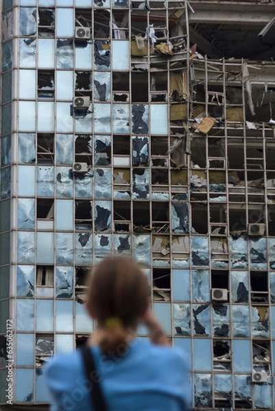 Fototapeta unrecognizable girl back to camera stands in front of building destroyed by unmanned aerial vehicle