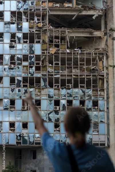 Fototapeta unrecognizable girl back to camera points at building destroyed by unmanned aerial vehicle. Civil infrastructure damaged by war drones. Selective focus