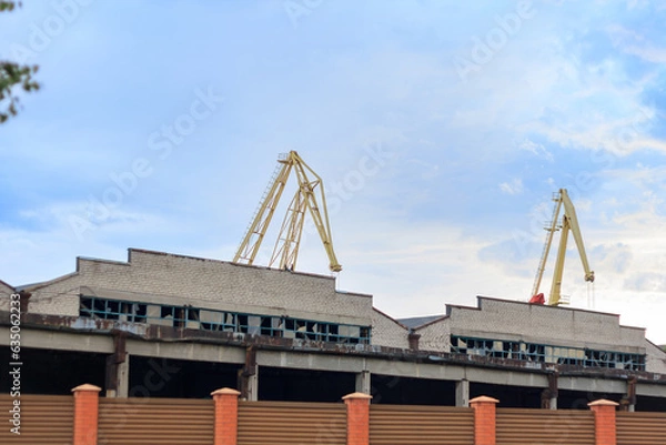 Fototapeta War in Ukraine 2023. Port building damaged by unmanned aerial vehicle. Infrastructure destroyed by military drone. Lifting cranes on background
