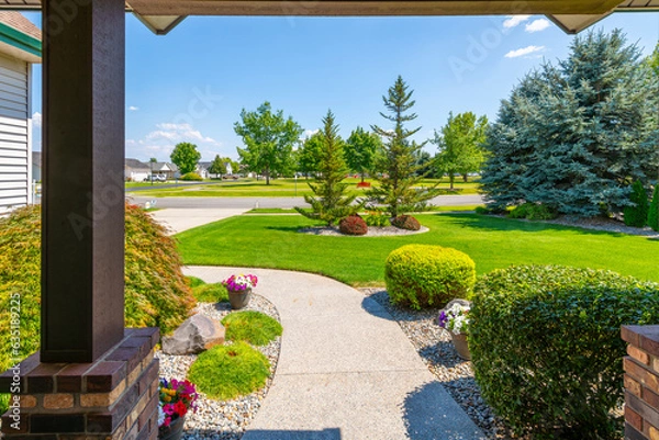 Fototapeta View from the front porch of a modern suburban home with a manicured front lawn in a nice community neighborhood across the street to a park on a sunny summer day.